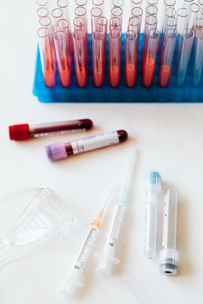 From above of transparent test tubes with colorful liquids placed on blue stand  and table near syringes and plastic eyeglasses